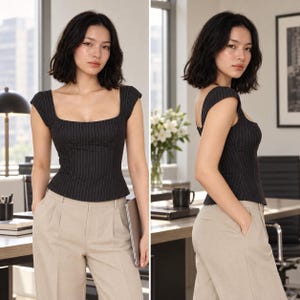 Op de afbeelding: Een zwart korset-stijl topje met krijtstreep, een vierkante halslijn en kapmouwtjes, gecombineerd met een beige broek met hoge taille. De top heeft verticale witte krijtstrepen, gestructureerde naden en een getailleerd lijfje.