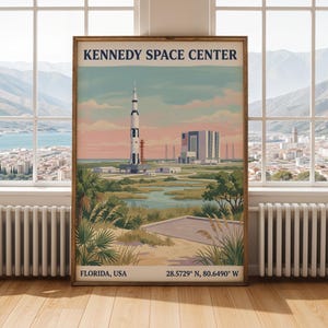 以下が含まれることがあります： フロリダ州ケネディ宇宙センターの様式化されたイラストが描かれた長方形のポスター。打ち上げ台に立つ高いロケット、大きな建物、海岸沿いの植生が柔らかな色調の空の下に描かれています。テキストには「KENNEDY SPACE CENTER」、「FLORIDA, USA」、「28.5729° N, 80.6490° W」と記されています。