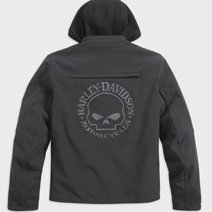 Puede incluir: Chaqueta negra con capucha y el logotipo de Harley-Davidson en la espalda. El logotipo es una calavera dentro de un círculo, con las palabras "HARLEY-DAVIDSON MOTORCYCLES" alrededor. La chaqueta tiene cremallera y un pequeño bolsillo.