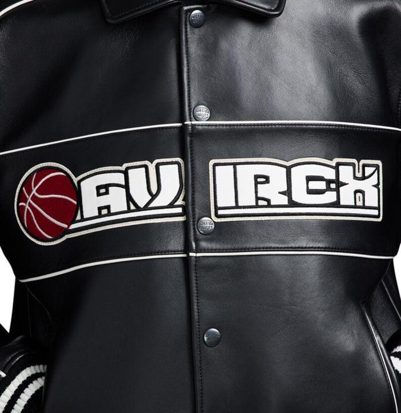 Puede incluir: Una chaqueta universitaria de cuero negro con una franja horizontal blanca en el pecho con el texto MAV IRCH en letras may&uacute;sculas blancas. Un gr&aacute;fico circular de un bal&oacute;n de baloncesto rojo se sit&uacute;a a la izquierda del texto. Botones de presi&oacute;n plateados.