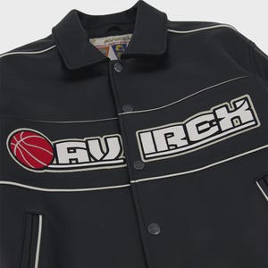 Puede incluir: Una chaqueta varsity negra con cuello blanco, cierre de botones a presi&oacute;n y detalles de ribetes blancos. El pecho muestra un gr&aacute;fico de baloncesto rojo y el texto bordado en blanco AVIRCK. La etiqueta interior dice AVIRCK AUTHENTIC VARSITY SPORTS.