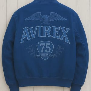 K&ouml;nnte beinhalten: Marineblaue Bomberjacke mit dem Wort "AVIREX" auf dem R&uuml;cken, &uuml;ber einem Schild mit der Zahl "75" und den Worten "WARRIORS WING". &Uuml;ber dem Wort "AVIREX" befindet sich ein Adler mit ausgebreiteten Fl&uuml;geln.