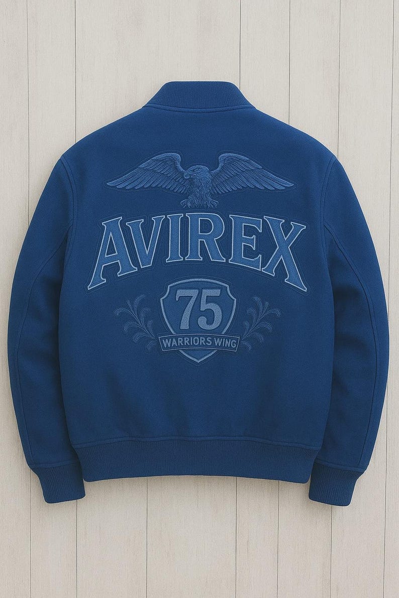 K&ouml;nnte beinhalten: Marineblaue Bomberjacke mit dem Wort "AVIREX" auf dem R&uuml;cken, &uuml;ber einem Schild mit der Zahl "75" und den Worten "WARRIORS WING". &Uuml;ber dem Wort "AVIREX" befindet sich ein Adler mit ausgebreiteten Fl&uuml;geln.