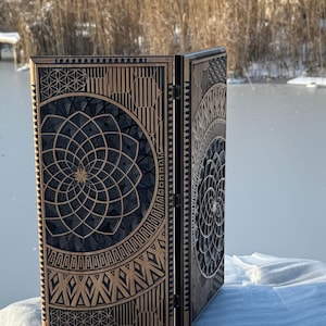 May include: A wooden backgammon set with intricate geometric designs. The set is open, revealing the playing surface and a collection of game pieces. The background shows a snowy landscape with a frozen lake and trees.
