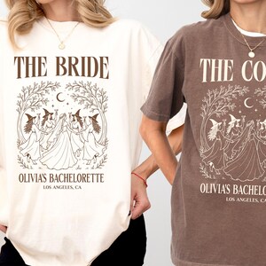 Op de afbeelding: Twee t-shirts met korte mouwen en ronde hals in ivoor en espressobruin. Het ivoorkleurige shirt heeft bruine tekst met THE BRIDE en OLIVIA'S BACHELORETTE LOS ANGELES, CA. Het espressokleurige shirt toont THE COVEN en OLIVIA'S BACHELORETTE LOS ANGELES, CA.