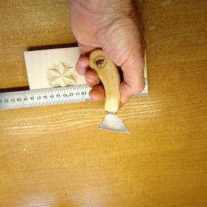May include: A wood carving tool with a wooden handle and a silver blade is held near a carved wooden star. The handle has the Bonobo Wood logo. A ruler with inch measurements is also visible.