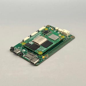 May include: A green Raspberry Pi Compute Module 3+ circuit board with various electronic components, including chips, connectors, and a micro SD card slot. The board is rectangular and has a smaller green board stacked on top.