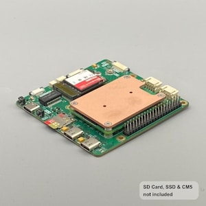 Puede incluir: Una placa de circuito verde con varios componentes electrónicos, incluyendo un disipador de calor color cobre, conectores y una tarjeta SD roja. La placa es rectangular y tiene múltiples puertos y chips. El texto en la parte inferior dice "SD Card, SSD & CM5 not included."