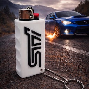 May include: White lighter case with black "STI" logo and a silver chain. A blue car is in the background with flames coming from the tyres. The STI logo is also in red at the top of the image.