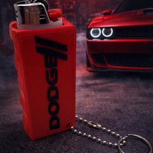 May include: Red lighter with the word "DODGE" printed in black. The lighter is attached to a silver chain and keyring. A red Dodge car is in the background.