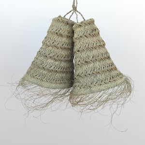 Puede incluir: Dos cestas tejidas en forma de campana cuelgan de una cuerda retorcida. Las cestas están hechas de fibras naturales de color marrón claro, con un patrón tejido y bordes deshilachados. El fondo es blanco liso.
