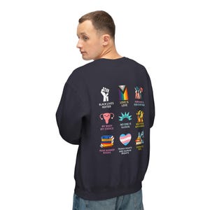 May include: Navy blue sweatshirt with various graphic icons and text, including "Black Lives Matter," a rainbow flag, and "Love is Love." Other graphics include a uterus, books, and a transgender pride flag. The sweatshirt is a comfortable, casual style.