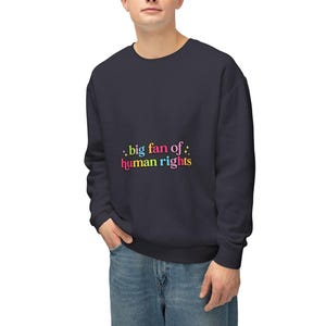 May include: Navy blue sweatshirt with the text ".big fan of: human rights" in colorful letters. The sweatshirt is a solid color and has a crew neck. The person in the image is wearing blue jeans.