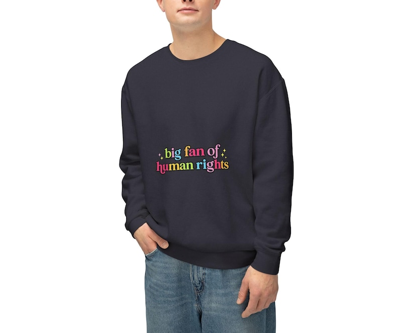 May include: Navy blue sweatshirt with the text ".big fan of: human rights" in colorful letters. The sweatshirt is a solid color and has a crew neck. The person in the image is wearing blue jeans.