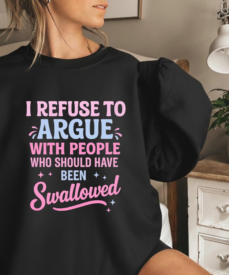 K&ouml;nnte beinhalten: Schwarzes Sweatshirt mit dem Text "I REFUSE TO ARGUE WITH PEOPLE WHO SHOULD HAVE BEEN Swallowed" in Rosa und Hellblau. Das Sweatshirt hat einen Rundhalsausschnitt und lange &Auml;rmel.