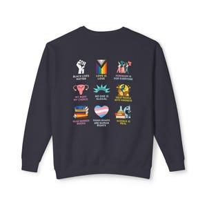 May include: Navy blue sweatshirt with nine colorful graphic designs. The designs include a raised fist, a rainbow flag, and the text "BLACK LIVES MATTER", "LOVE IS LOVE", and "FEMINISM IS FOR EVERYONE".