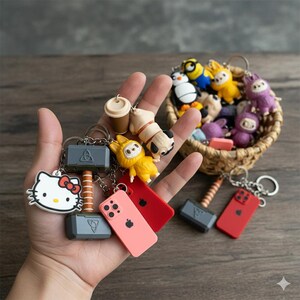 May include: A collection of colorful character keychains including a Hello Kitty face, a grey hammer, a coffee cup, a pug, and a red smartphone. Additional keychains featuring various cartoon figures are visible in a small woven basket.