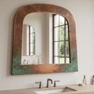 Puede incluir: Espejo arqueado grande con marco color cobre y pátina verde. El espejo está montado sobre un mueble de baño de madera con lavabo y grifo. El baño tiene una paleta de colores neutros y una ventana grande.