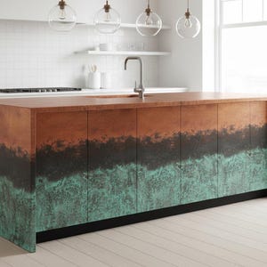 May include: A kitchen island with a copper countertop and a multi-toned facade. The copper surface transitions from a reddish-brown to a dark, almost black band, and then to a turquoise-green at the base. The island sits on a black base.