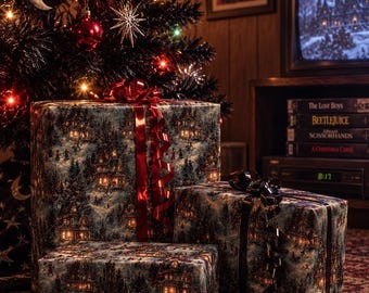 Könnte beinhalten: Drei rechteckige Geschenkboxen, eingewickelt in dunkles Papier mit einer winterlichen Dorfszene, beleuchteten Häusern und verschneiten Bäumen. Die größte Box hat ein glänzendes rotes Band, während die beiden kleineren Boxen schwarze Bänder tragen.