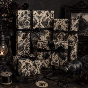 May include: Four rectangular gift boxes wrapped in cream-colored paper with a black damask pattern featuring hippos, moths, and bats. Each box is tied with black satin ribbon and includes a decorative gift tag with a moth or animal illustration.