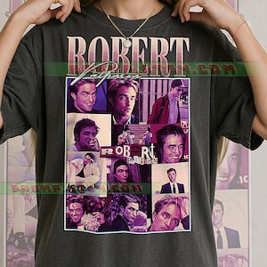 Op de afbeelding: Donkergrijs t-shirt met een collage van afbeeldingen van Robert Pattinson. Het shirt toont de naam "ROBERT PATTINSON" in een vintage stijl. De afbeeldingen zijn in een rasterpatroon gerangschikt.