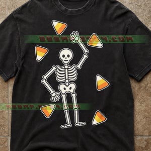 May include: Black t-shirt featuring a cartoon skeleton with outstretched arm and candy corn accents. The skeleton is white with black outlines, and the candy corn is orange, yellow, and white. The shirt has a vintage wash.
