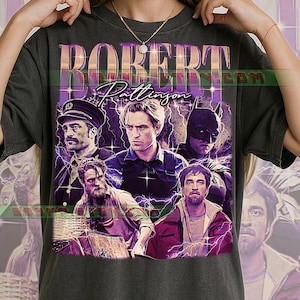 Op de afbeelding: Donkergrijs T-shirt met een vintage design met de naam Robert Pattinson en afbeeldingen van de acteur in verschillende rollen. Het ontwerp bevat paarse bliksemeffecten, waardoor een collage-effect ontstaat.