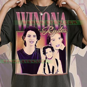 Könnte beinhalten: Dunkelgraues T-Shirt mit einem Retro-Grafikdesign von Winona Ryder. Das Design zeigt ihren Namen in Rosa über drei Bildern der Schauspielerin. Das T-Shirt hat einen klassischen Rundhalsausschnitt und kurze Ärmel.