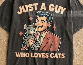 May include: Dark gray t-shirt with a retro graphic of a man holding a cat. The text reads "JUST A GUY WHO LOVES CATS" in a vintage font. The man is wearing a suit and tie, and the cat is gray and striped.