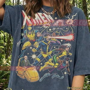 Peut inclure: T-shirt bleu denim avec un graphisme coloré des personnages de X-Men. Le design comprend Wolverine, Cyclope, Tornade, Malicia, et d'autres. Le t-shirt porte le mot "X-MEN" en haut et le mot "Denim" en bas.
