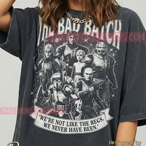 Könnte beinhalten: Dunkelgraues T-Shirt mit einer Grafik von Charakteren aus "The Bad Batch", dem Text "THE BAD BATCH" und einem Banner mit der Aufschrift "WE'RE NOT LIKE THE REGS. WE NEVER HAVE BEEN." Entworfen von TVKE.