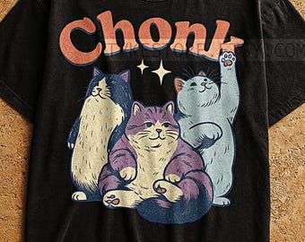 Może przedstawiać: Czarny t-shirt z retro wzorem. Słowo "Chonk" znajduje się nad trzema kreskówkowymi kotami w kolorze niebieskim, fioletowym i kremowym, z gwiazdkami. Koszulka ma wygląd vintage.