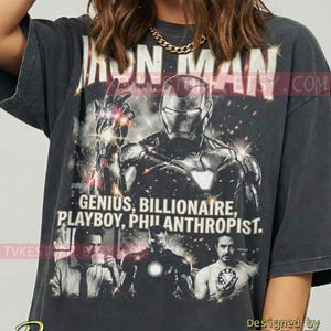 Könnte beinhalten: Dunkelgraues T-Shirt mit Iron Man-Motiv und dem Text "IRON MAN". Das Shirt enthält die Worte "GENIUS, BILLIONAIRE, PLAYBOY, PHILANTHROPIST." und Bilder der Figur.
