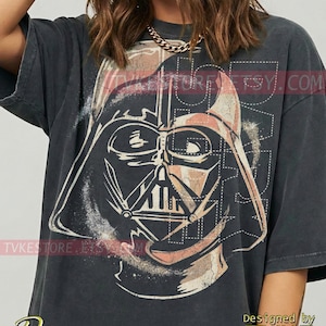 May include: Dark grey t-shirt with a distressed graphic of Darth Vader's helmet. The design incorporates beige and white tones, with the word "Pepper" in cursive at the bottom. The shirt has a vintage, worn appearance.