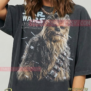 May include: Dark gray t-shirt featuring a graphic of Chewbacca from Star Wars: Episode V - The Empire Strikes Back. The shirt has the Star Wars logo and the text "Episode V" in a distressed style. The word "Pepper" is at the bottom.