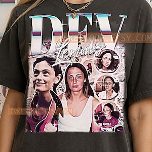 May include: Dark gray t-shirt featuring a graphic design with the word "DEV" in a holographic font, and the name "Lemon's" in a script font. The design includes multiple images of women. The Etsy shop URL is visible.