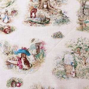 Puede incluir: Una tela blanca con un patrón repetido de personajes de Peter Rabbit, incluyendo Peter Rabbit, Benjamin Bunny y Mrs. Tiggy-Winkle. La tela presenta un fondo marrón claro con acentos verdes, azules y rojos.