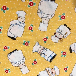 May include: Yellow fabric with a repeating pattern of white chefs wearing white hats and holding kitchen utensils. The background is a yellow polka dot pattern.