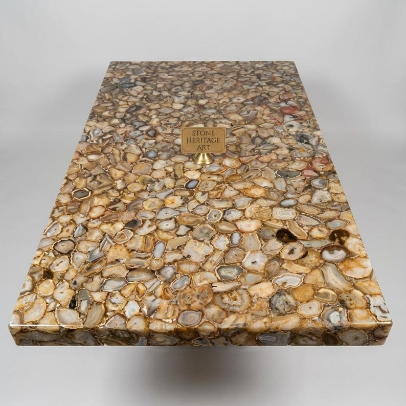 Puede incluir: Una mesa rectangular con una superficie hecha de piedras pulidas de forma irregular en tonos marrones, beige y grises. Un peque&ntilde;o letrero de lat&oacute;n que dice "STONE HERITAGE ART" est&aacute; fijado a la superficie de la mesa.