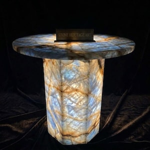 May include: A round, illuminated side table crafted from translucent stone with blue and amber veining. The table features a hexagonal base and a circular top, with a small rectangular plaque displaying the text STONE HERITAGE ART.