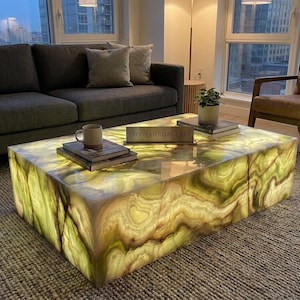 May include: A rectangular coffee table made of translucent green and white onyx stone with an internal light source that illuminates the natural veining. A small plaque on the surface displays the text STONE HERITAGE ART in gold lettering.