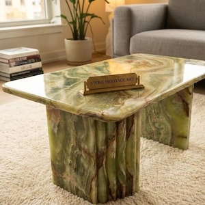 May include: A rectangular coffee table crafted from polished green onyx stone with natural veining and color variations. The table features a thick, smooth top and a fluted base. A small gold-toned nameplate sits on the surface with the text STONE HERITAGE ART.