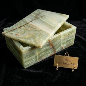 May include: A rectangular green stone box with a removable lid, featuring natural light green and white banding with thin brown veins. A small gold-toned metal sign stands in front, displaying the engraved text STONE HERITAGE ART.