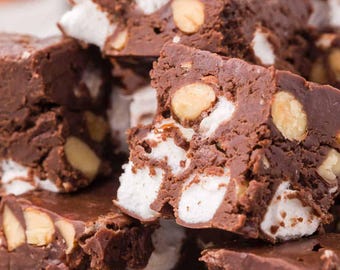 May include: Close-up of a stack of chocolate fudge squares. The fudge is a rich brown color and studded with white marshmallows and whole almonds. The dessert is stacked on top of each other.