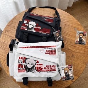 May include: Two messenger bags, one black and one white, with anime-style graphics and text. The bags have adjustable straps, front pockets, and buckle closures. Each bag features a character illustration and the word "CYBERPUNK" in red. Clear acrylic charms with character art are also visible.