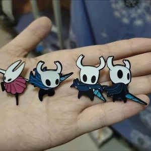 以下が含まれることがあります： 黒い目と角を持つ白いキャラクターが描かれた4つのエナメルピン。ピンク、青、黒など、さまざまな色のアクセントがあります。ジャケットやバッグに適した、小さくて詳細なピンです。