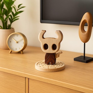 以下が含まれることがあります： 角のある頭と濃い茶色のマントを着たキャラクターの木製フィギュア。迷路のようなデザインの円形の台座に立っています。フィギュアは明るい木と濃い木で作られています。金色の時計と木製の彫刻も表示されています。