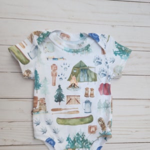 A lapneck bodysuit for infants featuring a canoe, tent, and various camping gear. Perfect for any camping trip.