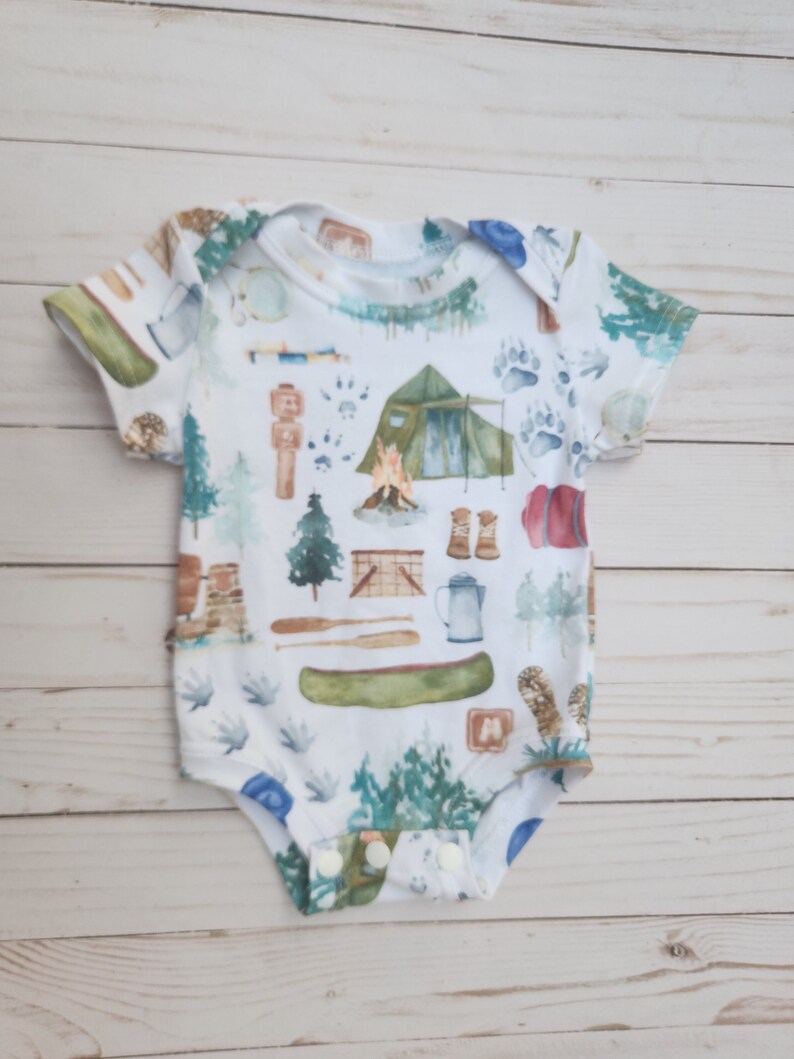 A lapneck bodysuit for infants featuring a canoe, tent, and various camping gear. Perfect for any camping trip.